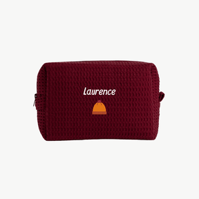 A black, waffle zippered pouch with the name Laurence and an embroidered beanie hat below the name on the front.