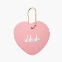 A pink heart charm. The pink heart charm has abbode written on the center The charm keychain has a gold key ring attached.