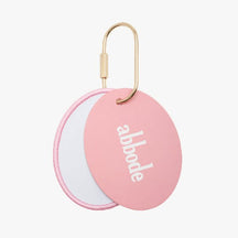 Oval charm keychain with a pink border and a white center and a pink oval charm. The pink oval charm has abbode written on the center The charm keychain has a gold key ring attached.