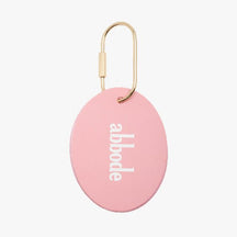 A pink oval charm. The pink oval charm has abbode written on the center The charm keychain has a gold key ring attached.